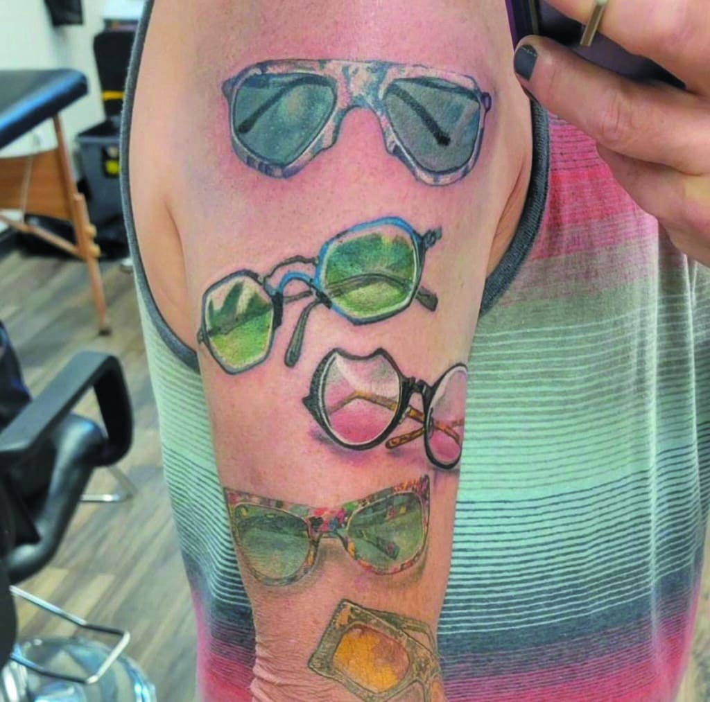 Photograph of an arm with several pairs of sunglasses tattooed on it.