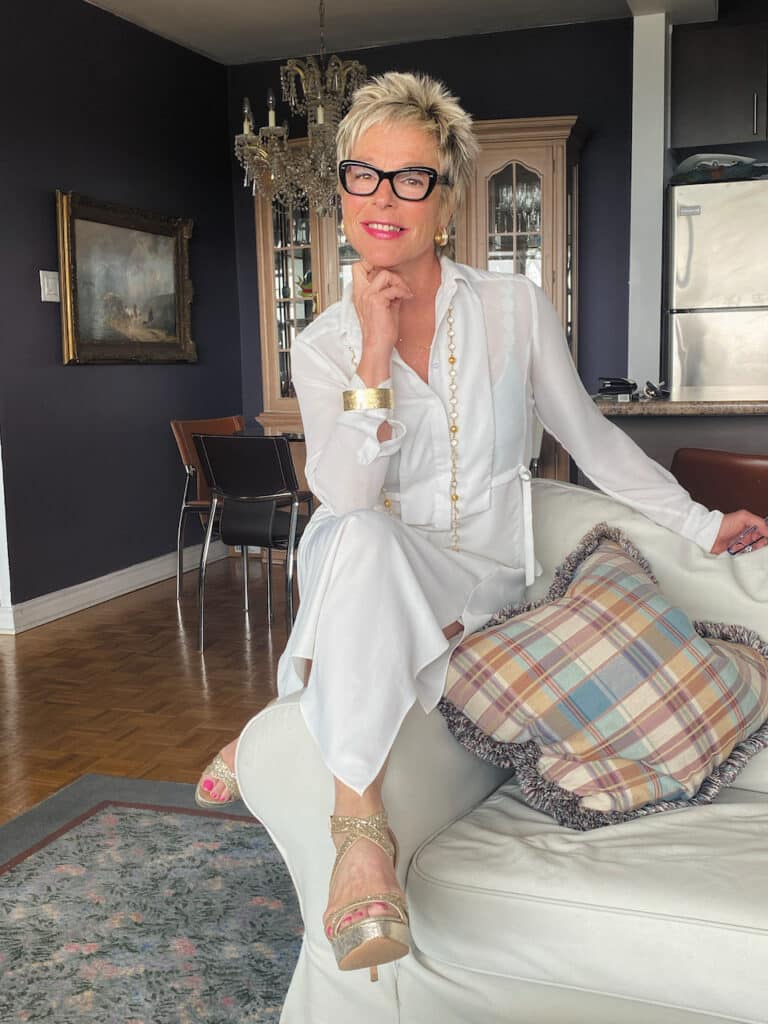 Photograph of Suzanne Sendel wearing all white, wearing chic glasses with large frames.