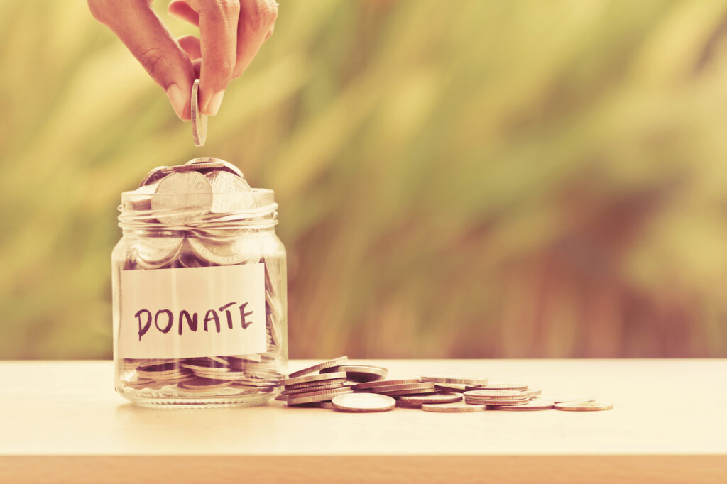 A hand placing a coin into a glass jar labeled 'DONATE', filled with coins, representing charitable giving for tax deductions.