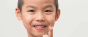 Close-up photograph of a smiling child holding a contact lens on the tip of their finger. Childhood myopia remedies include specialty contact lenses.